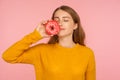 Portrait of fascinating hungry ginger girl in sweater smelling doughnut and expressing desire to eat sweet donut