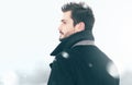 Portrait of fashion handsome man in winter snowstorm looks, profile view