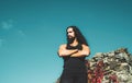 Portrait of fashion man model wearing dark clothes posing on blue sky background. Young strong muscular man standing on