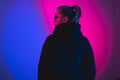 Portrait of fashion young girl in a black sweater with a hood and round sunglasses in red and blue neon light in the