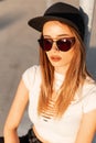 Portrait fashion young girl hipster with sexy lips in white torn top in fashionable sunglasses in black stylis baseball cap on sun Royalty Free Stock Photo