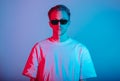 Portrait of fashion young man in white t-shirt and black sunglasses in red and blue neon light Royalty Free Stock Photo