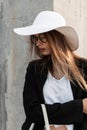 Portrait fashion young woman with handbag in beautiful stylish black-white clothes in summer straw hat in trendy glasses stands Royalty Free Stock Photo