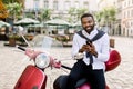 Portrait of fashionable African business man wearing white shirt and black pants, sitting on the red scooter in city Royalty Free Stock Photo