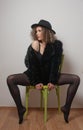 Portrait of a fashionable model with black fur sitting in a green chair in studio. Close up Portrait of young beautiful woman Royalty Free Stock Photo