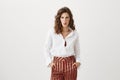 Portrait of fashionable slender european girl with curly hair, holding hands in pockets of striped pants, making faces