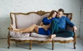Portrait of a fashionable stylish couple sitting together with bare feet on the couch in the living room, embracing, smiling,