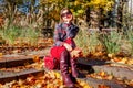 Portrait of fashionable woman wearing stylish blazer, skirt, knee high leather boots sitting in fall park with purse Royalty Free Stock Photo