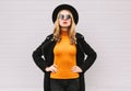 Portrait fashionable young blonde woman model wearing a black coat, round hat on gray background Royalty Free Stock Photo