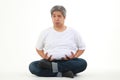 Portrait of a fat Asian man sitting on a white floor with his hands on his belly making a sad face.