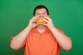 Portrait of a fat guy with a big hamburger in his hands, isolated on a green background. Chroma key, green screen