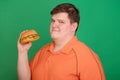 Portrait of a fat guy with a big hamburger in his hands, isolated on a green background. Chroma key, green screen