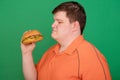 Portrait of a fat guy with a big hamburger in his hands, isolated on a green background. Chroma key, green screen