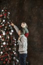 Portrait of father with little girl on Christmas Eve. Daughter sits on dads shoulders near beautiful Christmas tree. New Year mood