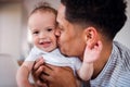 A portrait of father and small toddler son indoors at home, kissing.