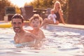 Portrait Of Father And Son Playing In Outdoor Pool On Vacation As Mother And Baby Watch From Side Royalty Free Stock Photo