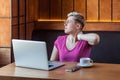 Portrait of feel bad tired young woman with short blonde hair in pink t-shirt and eyeglasses sitting in cafe and holding neck with Royalty Free Stock Photo