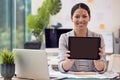 Portrait Of Female Architect Working In Office Sitting At Desk Holding Digital Tablet Towards Camera Royalty Free Stock Photo