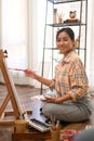 Portrait of female artist holding palette and painting picture on canvas with oil paints in cozy home studio Royalty Free Stock Photo