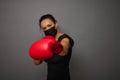 Portrait of female boxer wearing black medical mask and red boxing gloves, making direct hit. Woman boxer punching towards camera Royalty Free Stock Photo