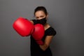 Young African woman boxer in black medical protective mask and red boxing gloves, punching towards camera, making direct hit, Royalty Free Stock Photo