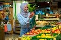 Portrait of a female buyer in a supermarket, a Muslim woman in a hijab chooses an apple fruit, happy with a large