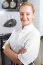 Portrait Of Female Chef Wearing Whites Standing By Cooker In Kit