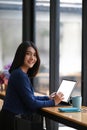 Portrait of female college student using tablet computer and smiling at camera while sitting in the library. Royalty Free Stock Photo