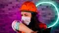 Portrait of female construction worker in overalls and medical mask coughing in elbow, being isolated at home against