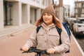 Portrait of female courier with big thermo backpack standing with electric scooter in city street looking at camera. Royalty Free Stock Photo