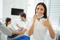 Portrait of female dentist showing thumb up while her collegue working with small client on the background