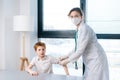 Portrait of female doctor applying plaster on shoulder of child boy after vaccination injection at hospital by window Royalty Free Stock Photo