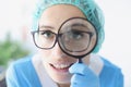 Portrait of female doctor in glasses looks through magnifying loupe