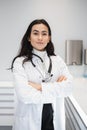 Portrait of female doctor in lab coat standing with crossed hands on her office. Royalty Free Stock Photo