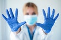 Female doctor with a medical mask showing hands to camera while wearing a blue nitrile gloves over white background Royalty Free Stock Photo