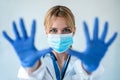 female doctor with a medical mask showing hands to camera while wearing a blue nitrile gloves over white background