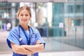 Portrait Of Female Doctor With Stethoscope Wearing Scrubs Standing In Modern Hospital Building Royalty Free Stock Photo