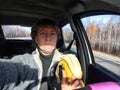 Portrait of female driver in solo journey. Adult mature middle aged woman holding steering wheel and banana. Eating