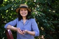 Portrait of a female farmer in a straw hat, smiles looking at camera and holding a handful of ripe harvested cherries