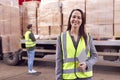 Portrait Of Female Freight Haulage Manager Standing By Truck Being Loaded By Fork Lift 