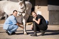 Portrait of female jockey and vet crouching by horse