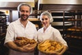 Portrait of female and male baker holding basket of bread and sweet food