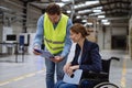 Portrait of female manager in wheelchair working in warehouse, talking with logistics employee. Concept of workers with Royalty Free Stock Photo