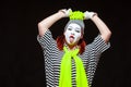 Portrait of female mime artist, isolated on black background. Young woman in striped clothes and funny bright hat shows Royalty Free Stock Photo