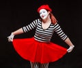 Portrait of female mime artist performing, isolated on black background. Woman in striped clothes holding her red skirt Royalty Free Stock Photo