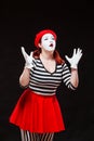 Portrait of female mime artist performing, isolated on black background. Woman in striped clothes and red skirt is Royalty Free Stock Photo