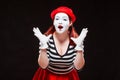 Portrait of female mime artist performing, isolated on black background. Woman in striped clothes and red skirt is Royalty Free Stock Photo