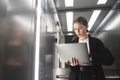 Portrait of a female office worker using her laptop in the elevator while being in hurry. Very busy businesswoman using her