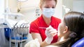 Portrait of female pediatric dentist inspecting girls teeth in dentist chair