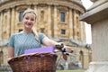 Portrait Of Female Student Riding Old Fashioned Bicycle Around Oxford University College Buildings By Radcliffe Camera In Royalty Free Stock Photo